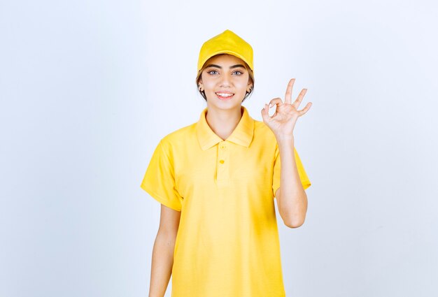 Mujer de entrega en uniforme amarillo de pie y mostrando gesto ok.
