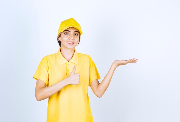 Mujer de entrega en uniforme amarillo de pie y mostrando la palma abierta.