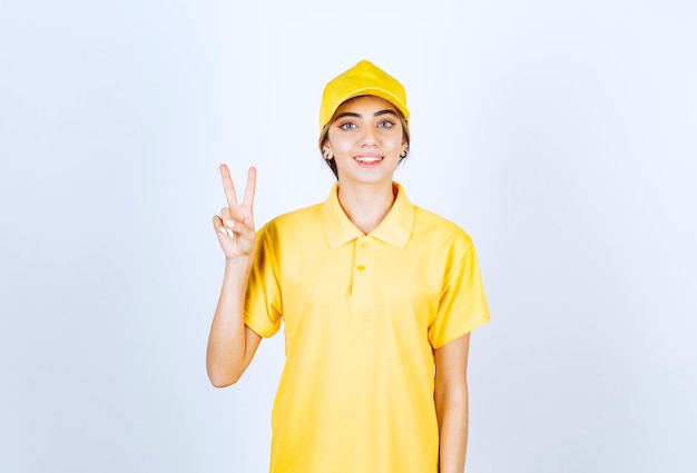 Mujer de entrega en uniforme amarillo de pie y mostrando el signo de la victoria.