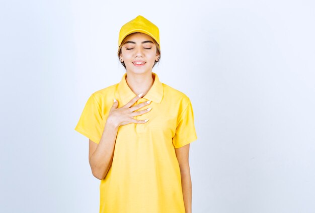 Mujer de entrega en uniforme amarillo de pie y posando con los ojos cerrados.
