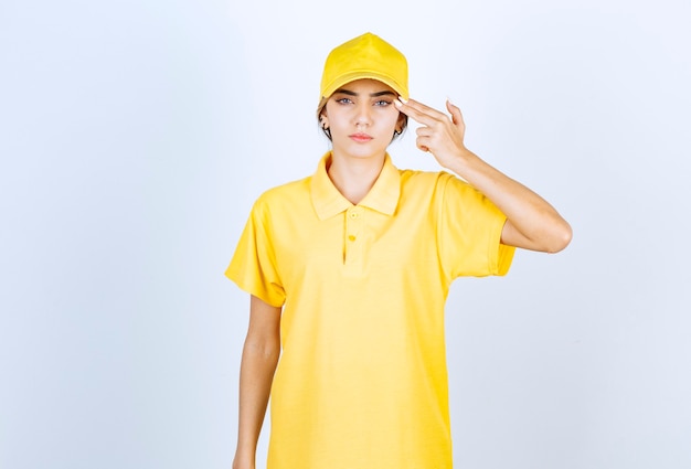 Mujer de entrega en uniforme amarillo sosteniendo dos dedos cerca de la sien como una pistola.