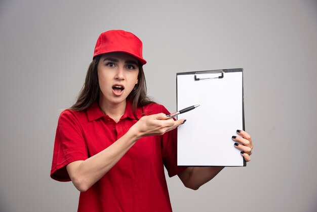 Mujer de entrega en uniforme rojo apuntando al portapapeles.