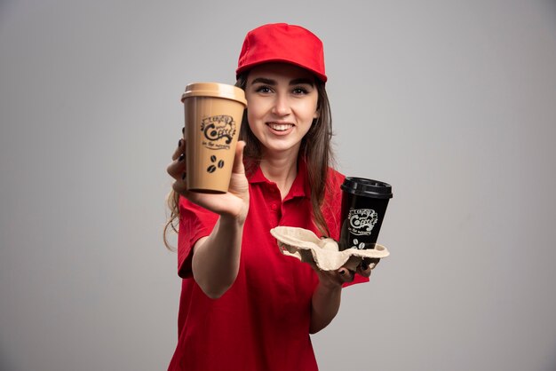 Mujer de entrega en uniforme rojo mostrando tazas de café.