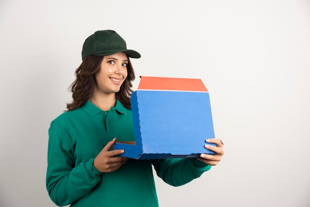 Mujer de entrega en uniforme verde con caja de pizza abierta.