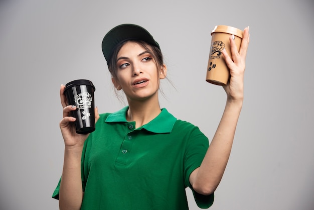 Mujer de entrega en uniforme verde mirando tazas de café