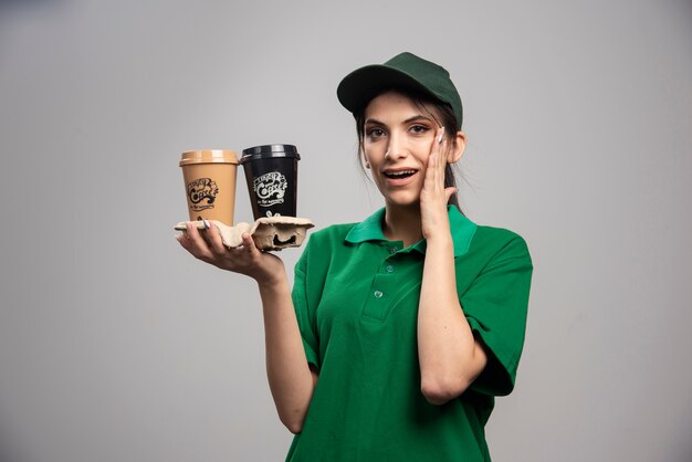 Mujer de entrega en uniforme verde de pie con tazas de café.