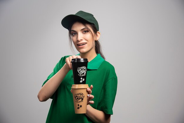 Mujer de entrega en uniforme verde posando con tazas de café