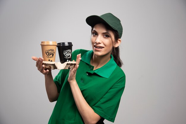 Mujer de entrega en uniforme verde posando con tazas de café.