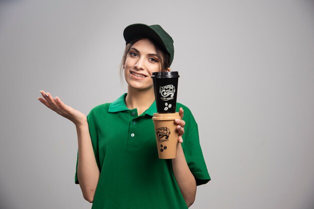 Mujer de entrega en uniforme verde sosteniendo tazas de café
