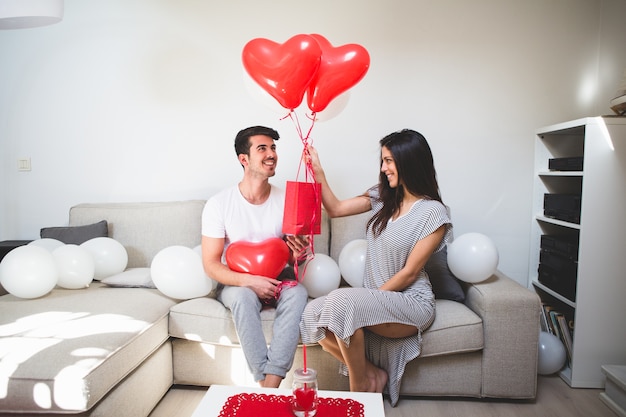 Foto gratuita mujer entregando a su novio globos y una bolsa roja