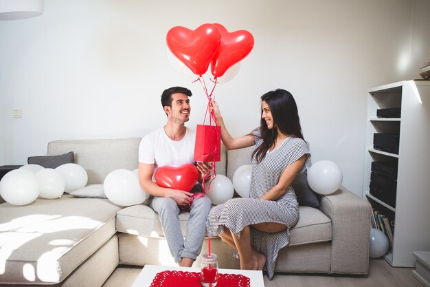 Mujer entregando a su novio globos y una bolsa roja