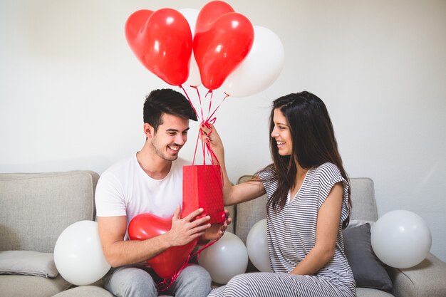 Mujer entregando a su novio globos y una bolsa roja