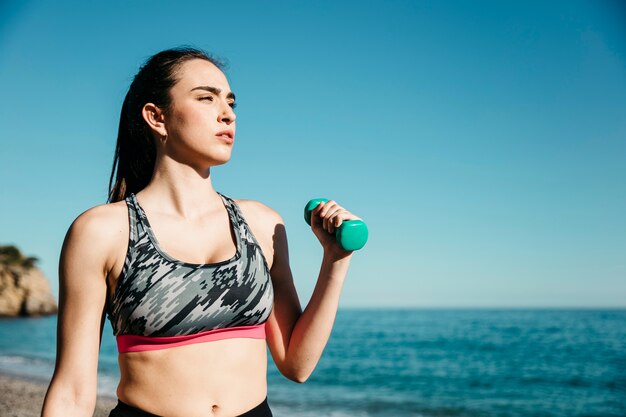 Mujer entrenando con pesas en playa soleada