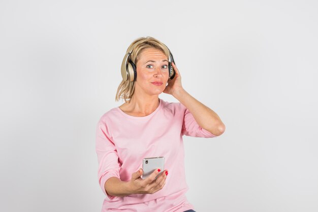 Mujer envejecida en blusa rosa con auriculares usando teléfono inteligente