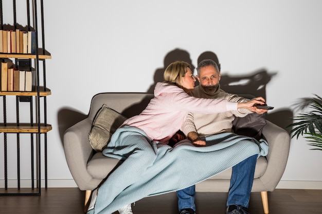 Mujer envejecida que detiene al hombre con el control remoto de la TV para cambiar el canal en la TV en el sofá