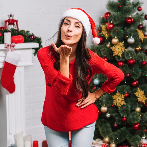 Mujer enviando beso al aire cerca de arbol de navidad