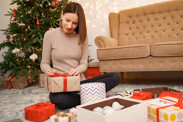 Mujer envolver el regalo de Navidad mientras está sentado en la carpa en la sala de estar