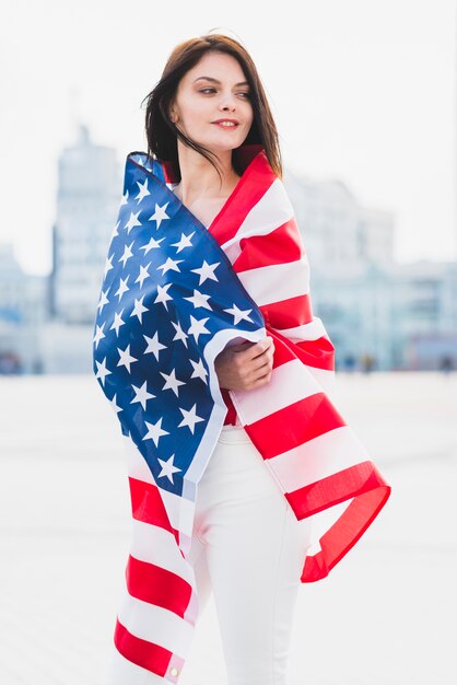 Mujer envuelta en bandera americana mirando patriotamente a lo largo de la plaza