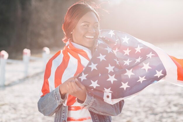 Mujer envuelta en bandera de Estados Unidos de pie sobre la arena