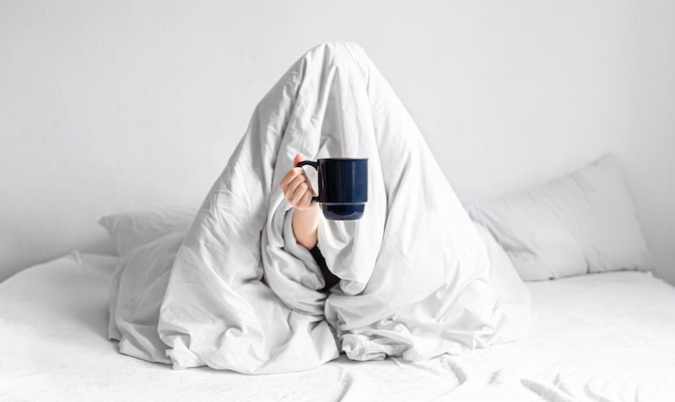 Foto gratuito una mujer envuelta en una manta se sienta en la cama con una taza de café en las manos.