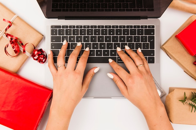 Mujer escribiendo en computadora portátil con cajas de Navidad en mesa