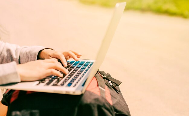 Mujer escribiendo en la computadora portátil colocada en las mochilas