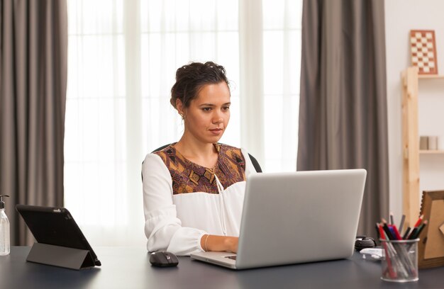 Mujer escribiendo en la computadora portátil mientras trabaja desde la oficina en casa.