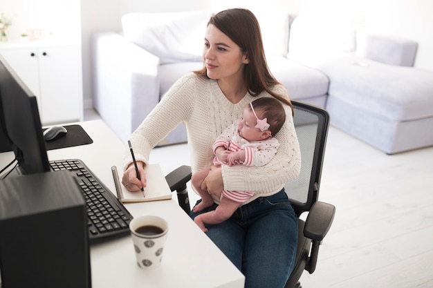 Mujer escribiendo y sosteniendo bebé