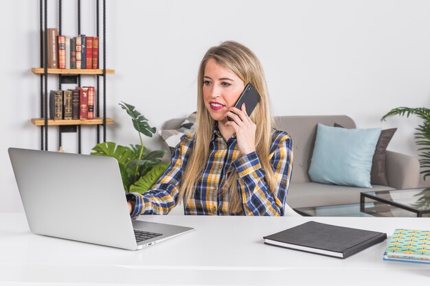 Mujer escribiendo en el teclado mientras habla por teléfono inteligente