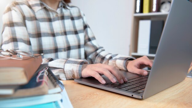 Mujer en escritorio y manos escribiendo en el teclado del ordenador portátil en la oficina en casa.