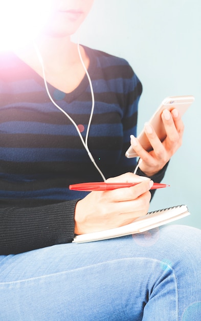 Mujer escuchando música por el auricular y mirar el teléfono inteligente en la mano con la pluma en la otra mano