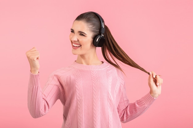 Mujer escuchando música en auriculares inalámbricos vistiendo un suéter rosa sonriendo feliz estado de ánimo positivo posando en rosa