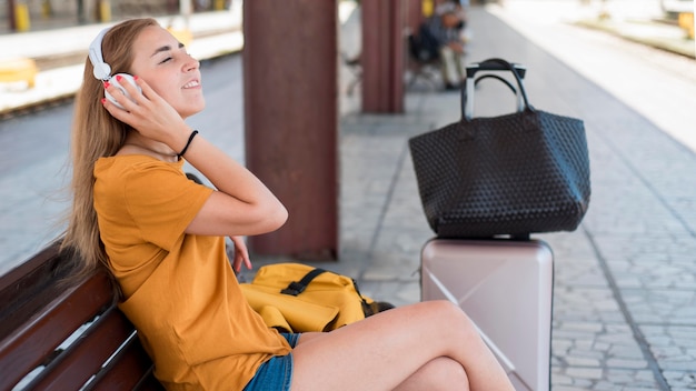 Foto gratuita mujer escuchando música en un banco en la estación de tren