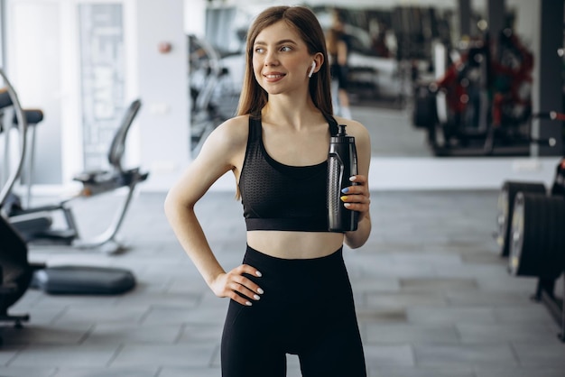 Mujer escuchando música y bebiendo agua en el gimnasio.