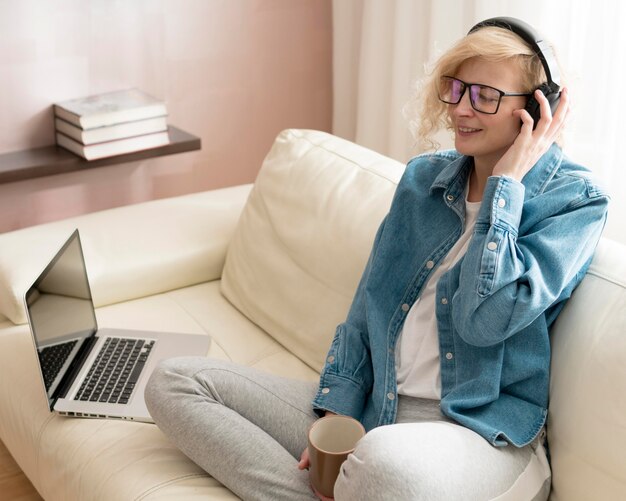 Mujer escuchando música y sosteniendo la taza de café en el sofá