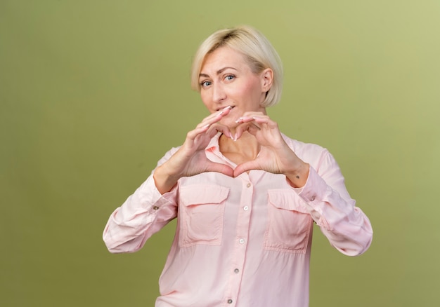 Mujer eslava rubia joven complacida que muestra el gesto del corazón