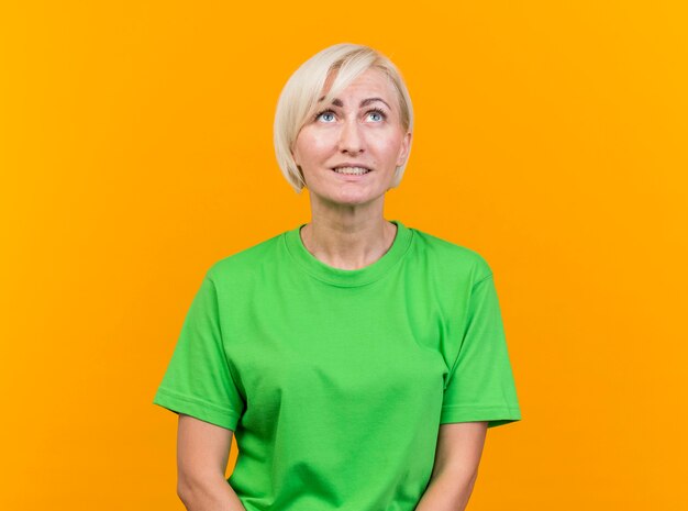 Mujer eslava rubia de mediana edad complacida mirando hacia arriba aislado sobre fondo amarillo con espacio de copia