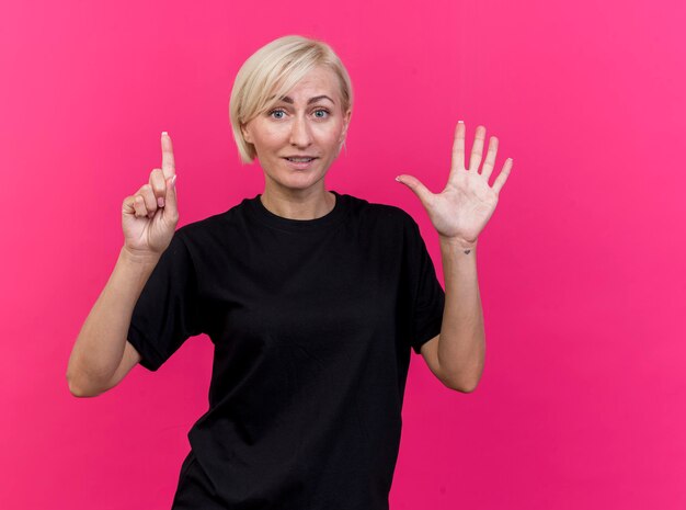 Mujer eslava rubia de mediana edad complacida que muestra seis con las manos mirando al frente aislado en la pared rosa con espacio de copia