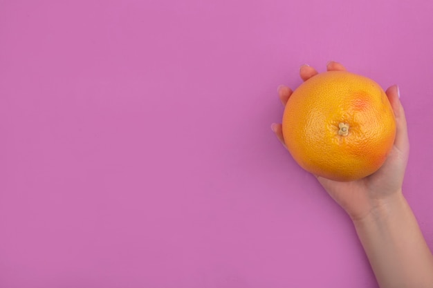 La mujer del espacio de copia de la vista superior sostiene en la mano pomelo sobre fondo rosa