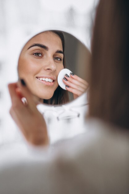 Mujer con espejo quitando maquillaje con almohadilla