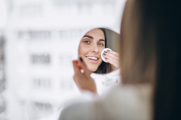 Mujer con espejo quitando maquillaje con almohadilla