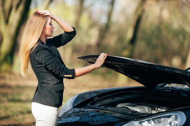 Una mujer espera ayuda cerca de su automóvil averiado al costado de la carretera.