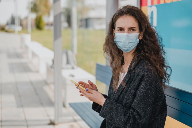 Mujer esperando el autobús y sosteniendo su teléfono móvil