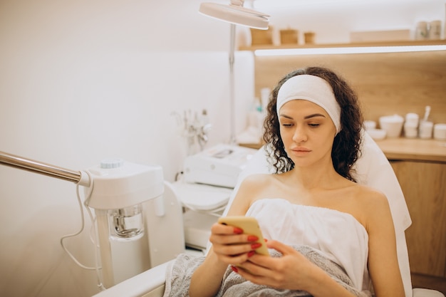 Mujer esperando en cosmetóloga y usando teléfono