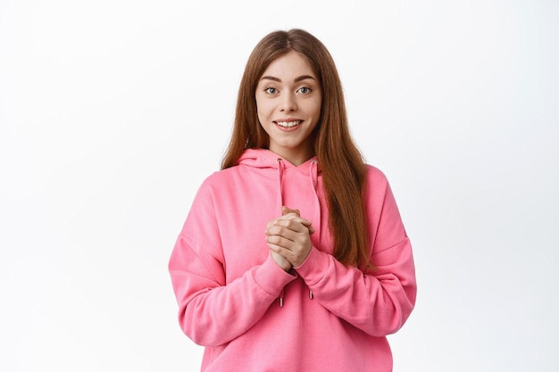 Mujer esperanzada aprieta las manos y sonríe a la cámara, anticipando algo, mirar agradecido, expresar gratitud, fondo blanco.