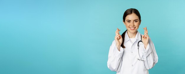 Foto gratuita mujer esperanzada, doctora, trabajadora de laboratorio, cruza los dedos y sonríe rezando pidiendo un deseo anticipando estar de pie