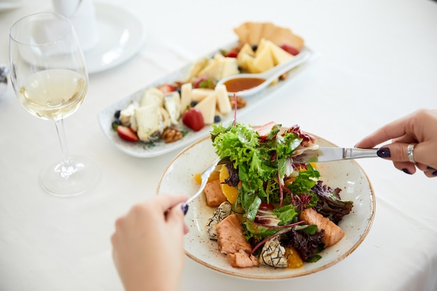 mujer está comiendo ensalada de cerdo con lechuga, queso y una copa de vino