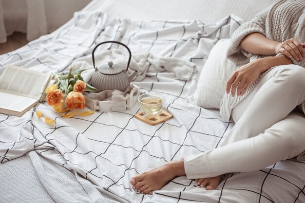 La mujer está descansando en la cama con té, un libro y un ramo de tulipanes