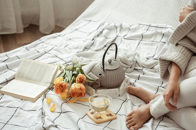 La mujer está descansando en la cama con té, un libro y un ramo de tulipanes