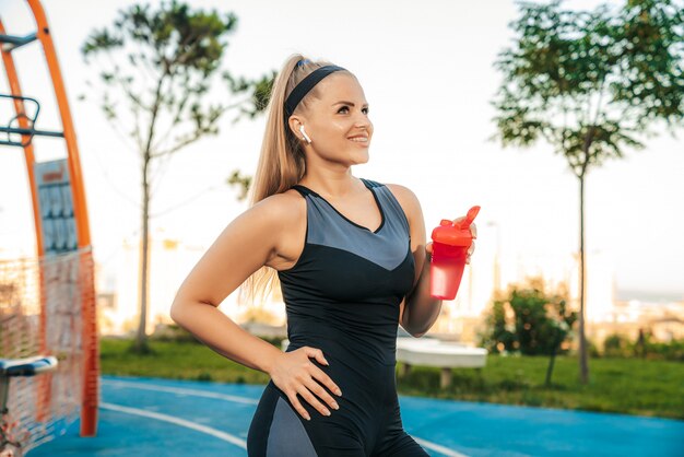 Mujer está parada en el gimnasio al aire libre con una botella de agua